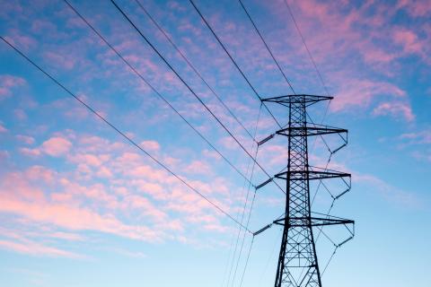 A high-voltage power line stanchion in silhouette again a blue sky with pink clouds